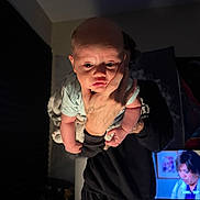 Eloise is registered to the contest to win money with this photo: baby, infant, person, hand, face, indoor, lighting, expression, adult, television, screen, shadow, clothing, blanket, tattoo, holding, portrait, curious, wide_eyes, young_child