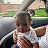 baby, child, infant, person, car_interior, car_window, seat, hand, clothing, shorts, shirt, pout, curly_hair, skin, face, window_crack, outside_view, grass, building, parking