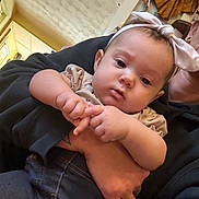 Azilynn is registered to the contest to win money with this photo: baby, child, headband, pink_bow, hand, tattoo, adult, indoor, curious_expression, clothing, denim, skin, portrait, person, holding, casual, face, cute, closeup, young