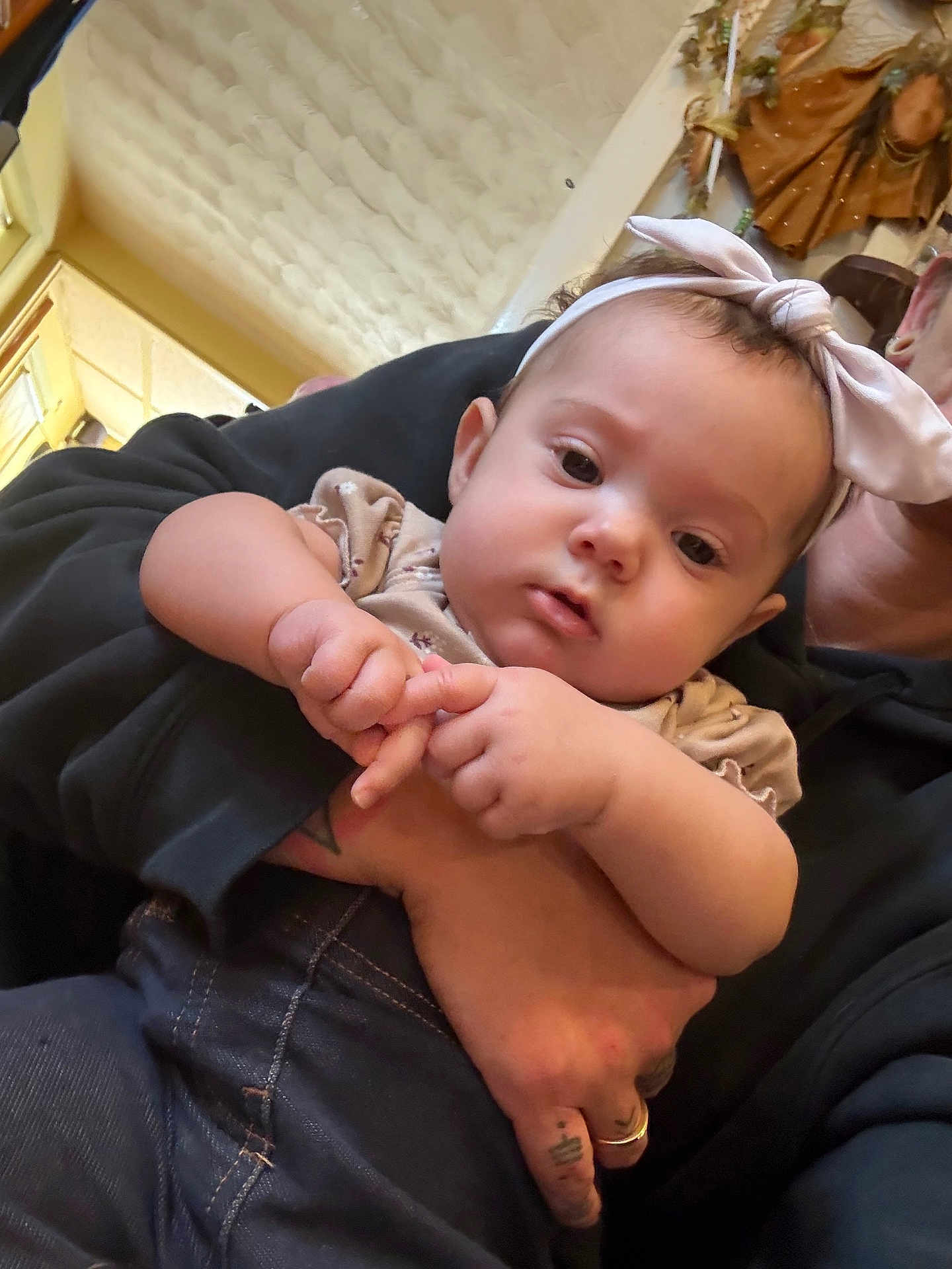 Azilynn is registered to the contest to win money with this photo: baby, child, headband, pink_bow, hand, tattoo, adult, indoor, curious_expression, clothing, denim, skin, portrait, person, holding, casual, face, cute, closeup, young
