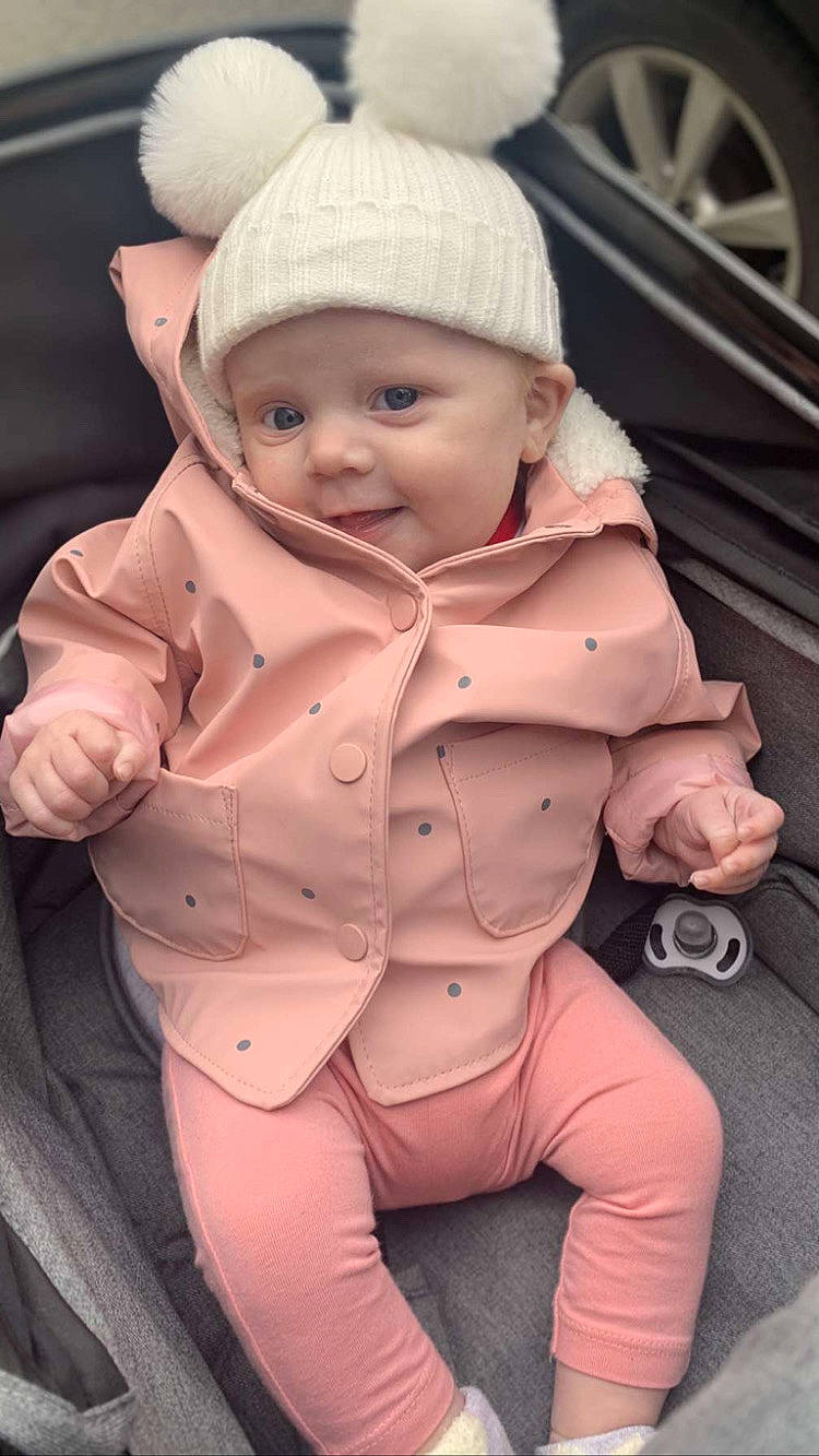 Bella-blu is registered to the contest to win money with this photo: baby, baby_carriage, baby_toddler_clothing, cap, cheek, dress, eye, finger, gesture, hand, headgear, headwear, jacket, lip, mouth, nose, outerwear, person, pink, skin