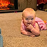 Elly is registered to the contest to win money with this photo: baby, child, infant, pink_dress, carpet, floor, indoor, fireplace, warm_light, cute, smiling, fingers_in_mouth, crawling, home, cozy, person, young_child, blond_hair, cheerful, relaxed