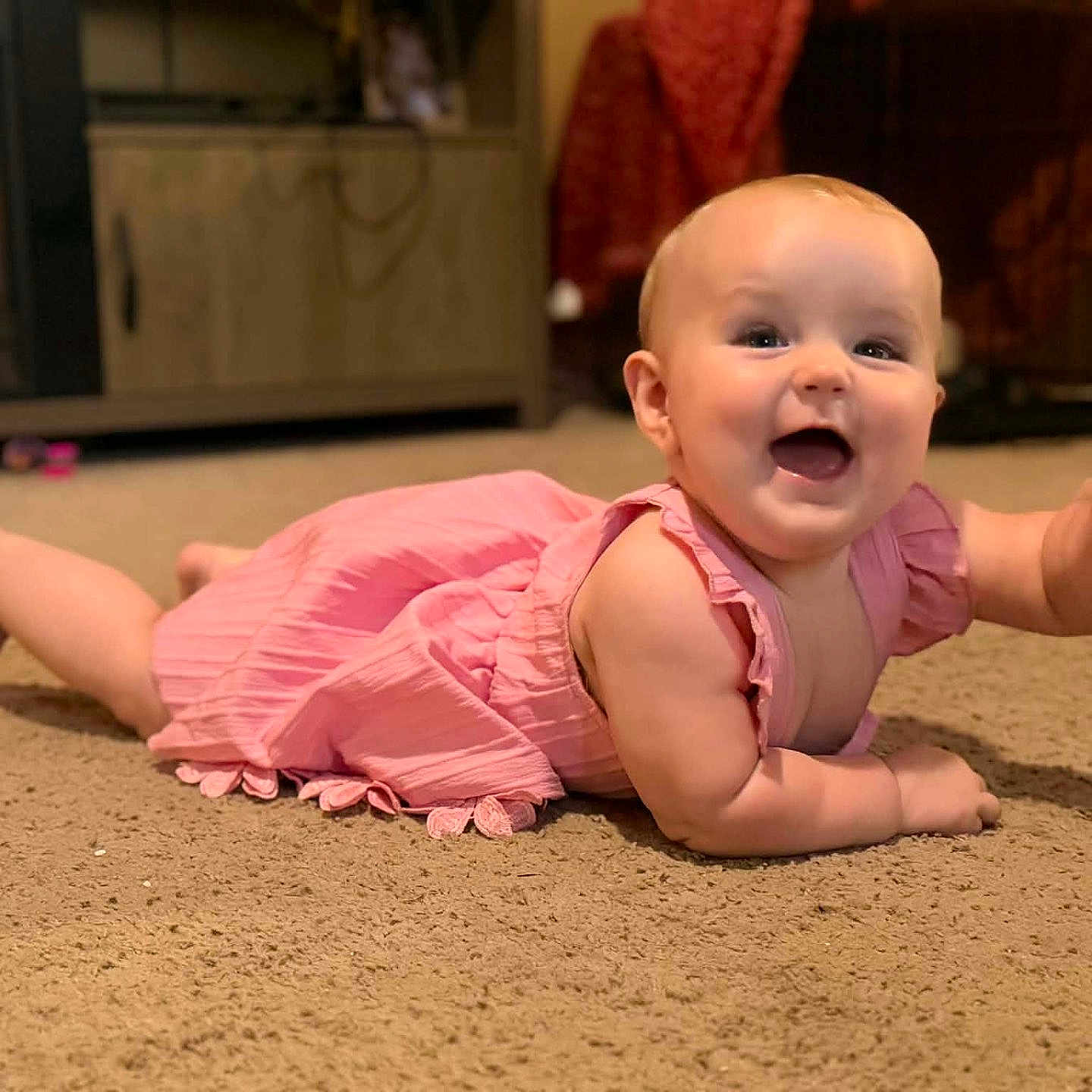 Elly is registered to the contest to win money with this photo: baby, pink_dress, carpet, indoor, smiling, happy, crawling, fireplace, warm, cozy, child, cute, infant, home, floor, person, waving, cheerful, living_room, portrait