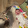 baby, dog, smiling, lying_down, fluffy_dog, white_onesie, colorful_mat, rug, wooden_floor, indoor, pet, child, cute, happy, cozy, animal, infant, playtime, floor, resting
