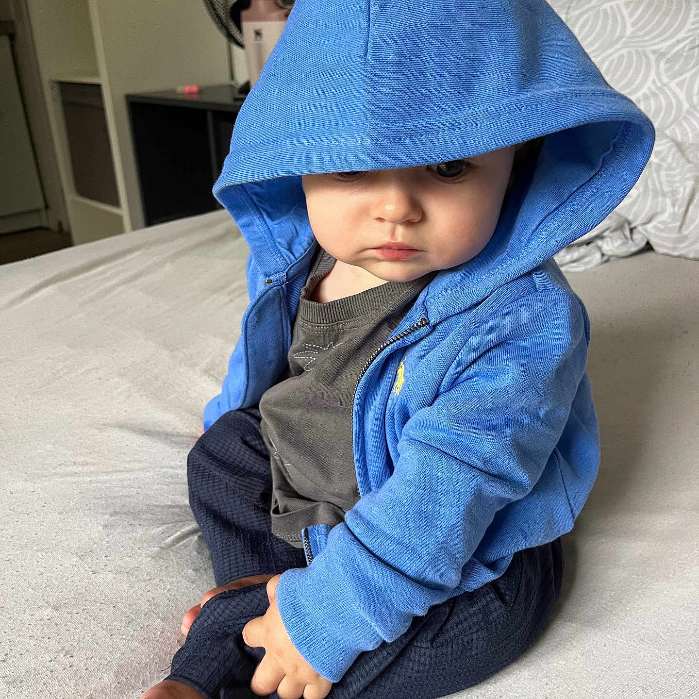 Eden participe au concours pour gagner de l'argent avec cette photo : baby, bed, blue_clothing, casual, child, clothing, curious, cute, fan, foot, furniture, hoodie, indoor, person, portrait, relaxed, shelf, sitting, toddler, young_child