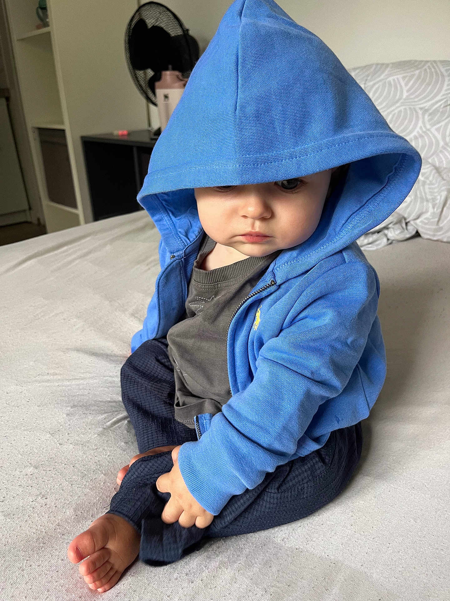 Eden participe au concours pour gagner de l'argent avec cette photo : baby, bed, blue_clothing, casual, child, clothing, curious, cute, fan, foot, furniture, hoodie, indoor, person, portrait, relaxed, shelf, sitting, toddler, young_child