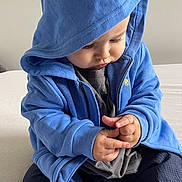 Eden participe au concours pour gagner de l'argent avec cette photo : baby, bed, blue_hoodie, casual_clothing, child, cozy, cross_legged, cute, focused, hands, hood, indoors, infant, neutral_background, portrait, sitting, skin, soft_lighting, toddler, young_child