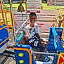 bell, blue, boy, child, clothing, daylight, fun, metal, outdoor, playground, safety, sandals, seat, shorts, sign, smiling, train_ride, tshirt, warning_sign, yellow