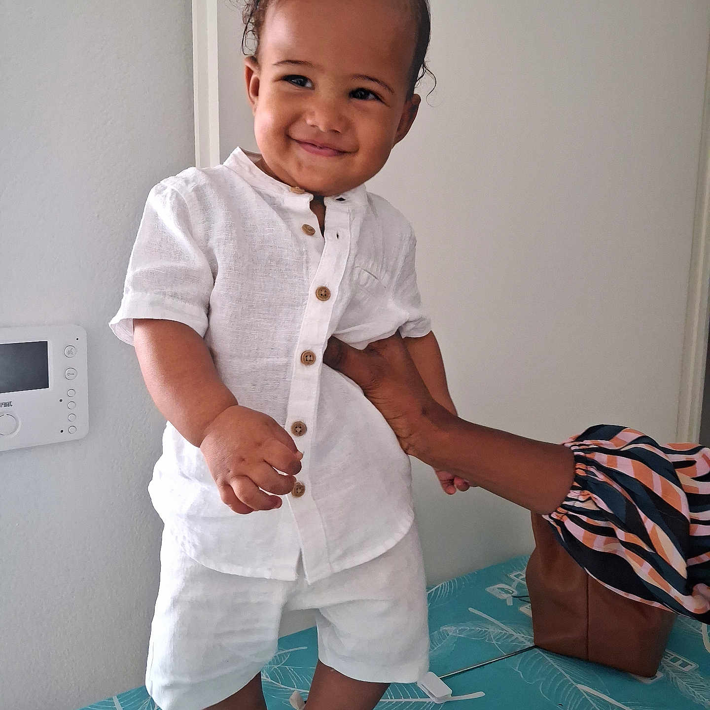 Timaël participe au concours pour gagner de l'argent avec cette photo : baby, brown_skin, buttoned_shirt, child, curly_hair, cute, hand, happy, indoor, joy, patterned_surface, person, shoes, shorts, smile, standing, support, toddler, white_clothing, young_child