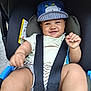 baby, blue_cap, car_seat, cheerful, child, clothing, cute, happy, headwear, infant, outdoor, person, playful, portrait, safety_harness, seatbelt, small_child, smiling, striped_shorts, toddler