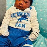 Darion is registered to the contest to win money with this photo: newborn, baby, infant, child, portrait, lying_down, football_fan, sportswear, blue_clothing, white_clothing, cap, mittens, socks, cushion, blanket, stars, indoor, smiling, face, photography