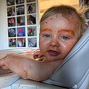 Hudson is registered to the contest to win money with this photo: baby, messy, food, high_chair, blue_eyes, face, arm, indoor, photography, child, curious, skin, hair, family_photos, background, smudge, seat, expression, person, home