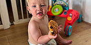 Hudson is registered to the contest to win money with this photo: baby, toddler, child, diaper, floor, wooden_floor, toy, baby_walker, indoor, pastry, chocolate, food, sitting, cute, smiling, happy, playful, face, person, home