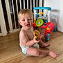 baby, toddler, child, diaper, floor, wooden_floor, toy, baby_walker, indoor, pastry, chocolate, food, sitting, cute, smiling, happy, playful, face, person, home