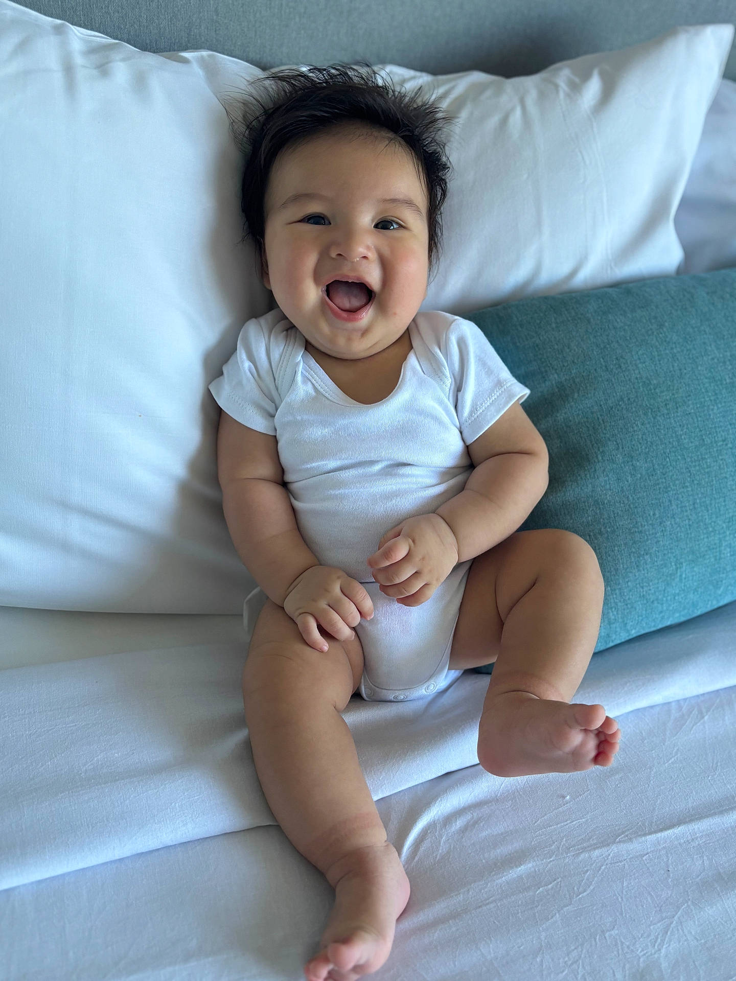 Jacob is registered to the contest to win money with this photo: baby, bed, blue_pillow, child, cute, expression, face, feet, hair, hands, happy, indoor, infant, person, pillow, sitting, skin, smiling, white_clothing, young