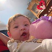 Rose is registered to the contest to win money with this photo: baby, child, woman, plush_toy, indoor, cabinet, heart_decoration, furniture, person, smile, face, closeup, soft_toy, curly_hair, sweater, room, home, family, happy, portrait