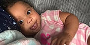Noelani is registered to the contest to win money with this photo: baby, infant, child, pink_clothing, blanket, couch, smile, face, eyes, hand, soft_texture, indoor, relaxing, cute, cozy, curly_hair, portrait, comfortable, toddler, lying_down