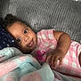 baby, infant, child, pink_clothing, blanket, couch, smile, face, eyes, hand, soft_texture, indoor, relaxing, cute, cozy, curly_hair, portrait, comfortable, toddler, lying_down