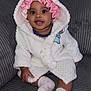 Noelani is registered to the contest to win money with this photo: baby, child, smiling, sitting, robe, hood, bonnet, pink, white, couch, furniture, indoors, happy, cute, infant, person, sock, clothing, face, portrait