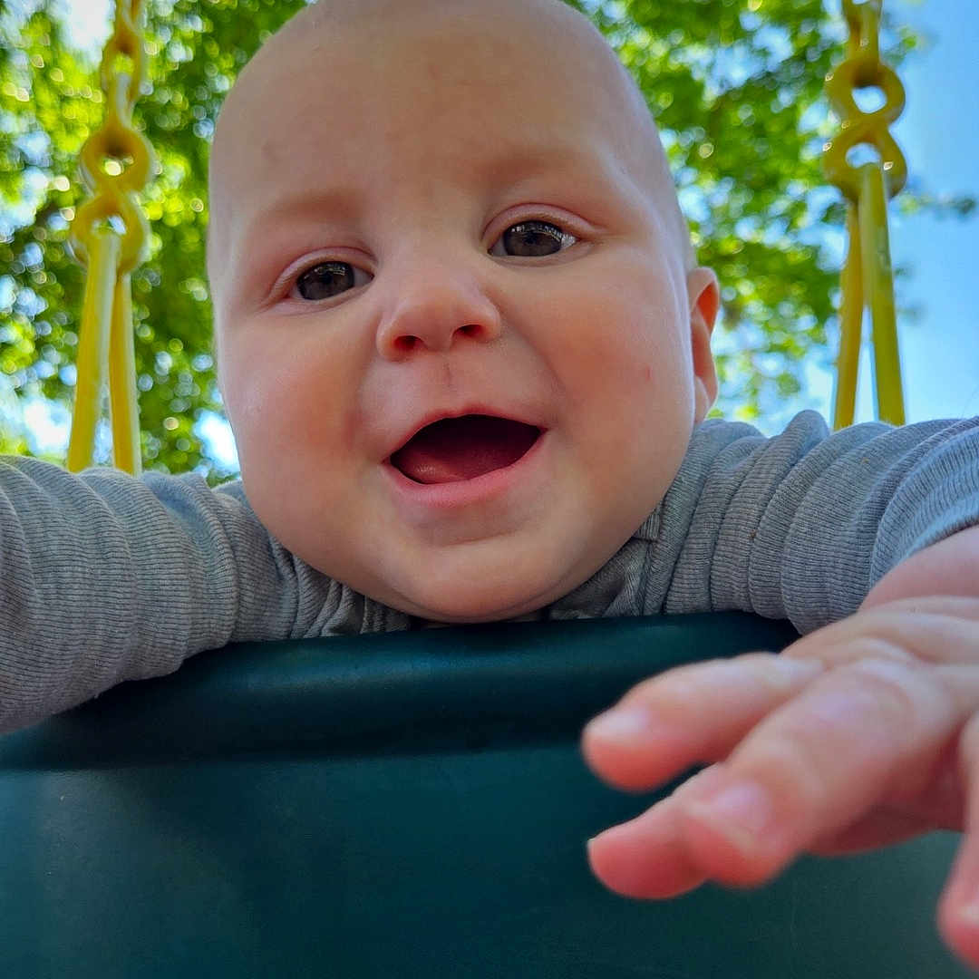 Roman is registered to the contest to win money with this photo: baby, bodypart, face, finger, grass, hand, happy, head, nature, outdoorplayarea, outdoors, park, person, photography, plant, playarea, portrait, swing, toy, tree