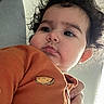 Kianna is registered to the contest to win money with this photo: baby, child, infant, portrait, close_up, curly_hair, serious_expression, pout, orange_clothing, onesie, smiling, face, eyes, nose, mouth, hand, indoor, window, natural_light, photography