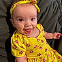 Zara is registered to the contest to win money with this photo: baby, child, smiling, yellow_dress, headband, flower_pattern, happy, sitting, couch, cushion, portrait, indoors, cute, face, eyes, tongue_out, person, apparel, infant, bright_colors