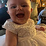 Saoirse is registered to the contest to win money with this photo: baby, child, smiling, dress, white_dress, indoor, party, celebration, person, happy, face, portrait, people, event, blurred_background, infant, cute, toddler, formal_wear, fun