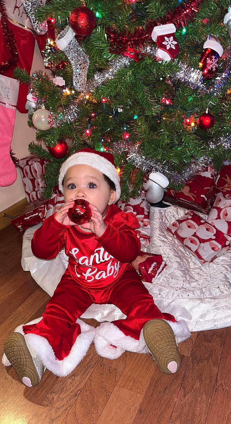 Alani is registered to the contest to win money with this photo: baby, baby_toddler_clothing, christmas, christmas_decoration, christmas_ornament, christmas_tree, dress, event, eye, happy, headwear, holiday, holiday_ornament, human_body, lap, ornament, person, plant, sleeve, toddler