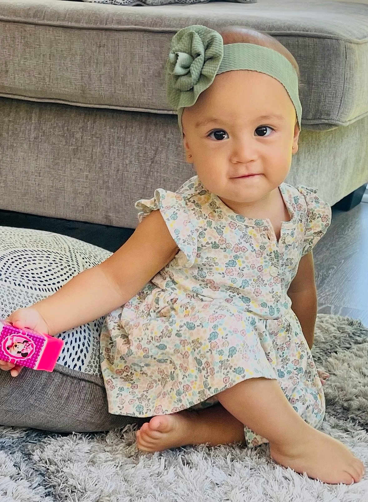 Jovana is registered to the contest to win money with this photo: toddler, child, girl, floral_dress, headband, flower, toy, pink, carpet, rug, couch, indoor, furniture, barefoot, smiling, sitting, cute, playful, young_child, home