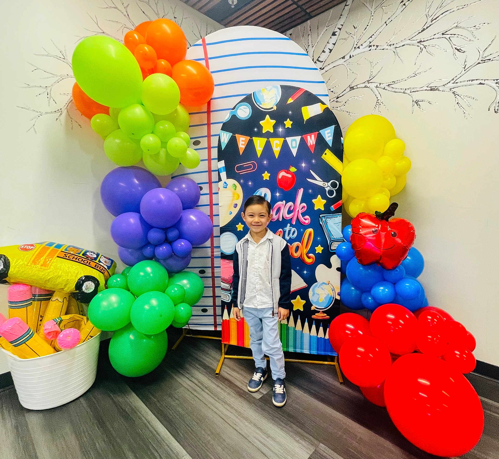 Jovan is registered to the contest to win money with this photo: child, boy, balloons, backdrop, school_theme, colorful, indoor, smiling, casual_clothing, flooring, wall, decorations, celebration, event, young_person, portrait, standing, happy, party, school_bus_balloon