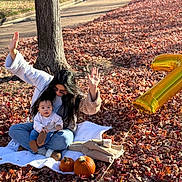 Miranda Castro joined the competition — help win amazing prizes! baby, woman, autumn, leaves, pumpkin, balloon, blanket, outdoor, park, tree, fall, celebration, number_balloon, casual_clothing, sitting, sunlight, shade, nature, playful, family