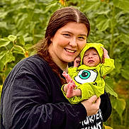 Waylon joined the competition — help win amazing prizes! woman, baby, child, sunflower, flower, green_clothing, outdoor, nature, smile, holding, portrait, plants, field, happy, person, infant, headwear, bright_colors, grass, casual_clothing