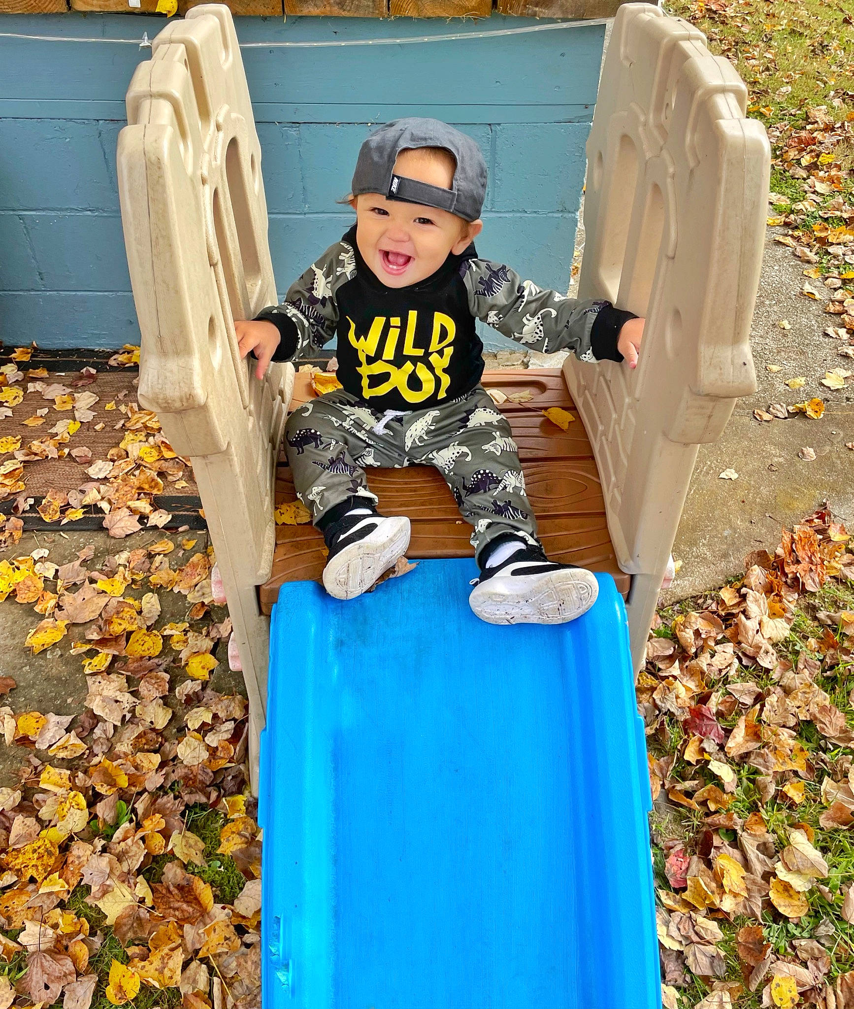 Sander is registered to the contest to win money with this photo: baseball_cap, boot, child, fun, games, grass, headwear, leisure, outdoor_play_equipment, people_in_nature, person, personal_protective_equipment, play, playground, playground_slide, public_space, recreation, sitting, sneakers, soil