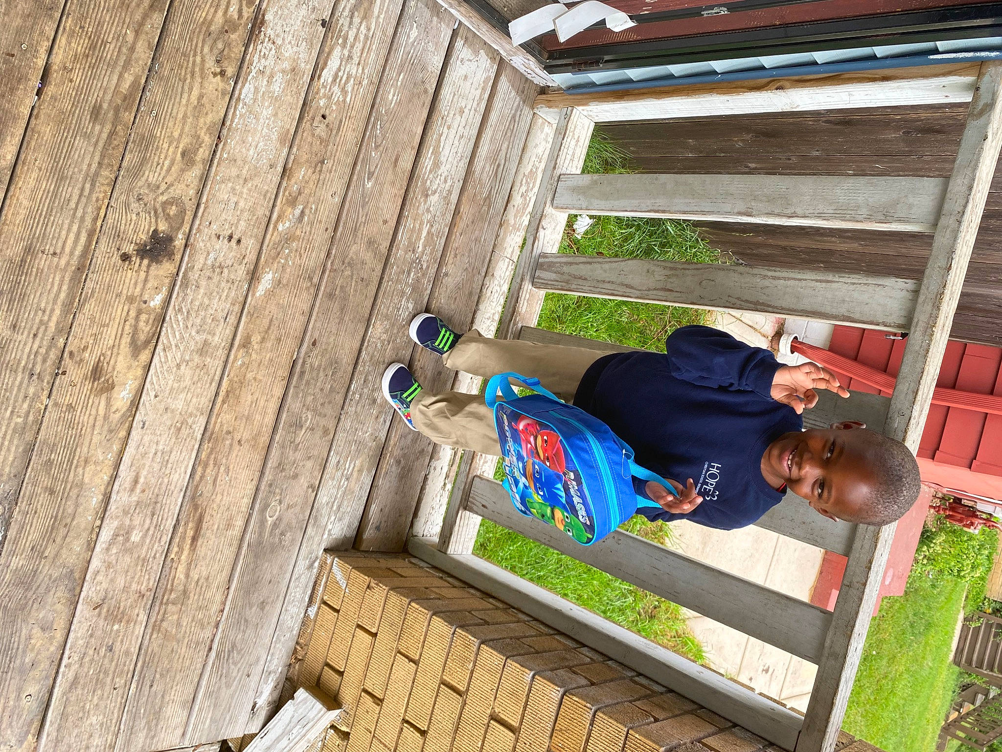 Malachi is registered to the contest to win money with this photo: child, comfort, deck, flooring, fun, grass, hardwood, house, joy, leisure, lumber, person, plank, plant, plywood, shorts, sitting, t_shirt, toddler, tree