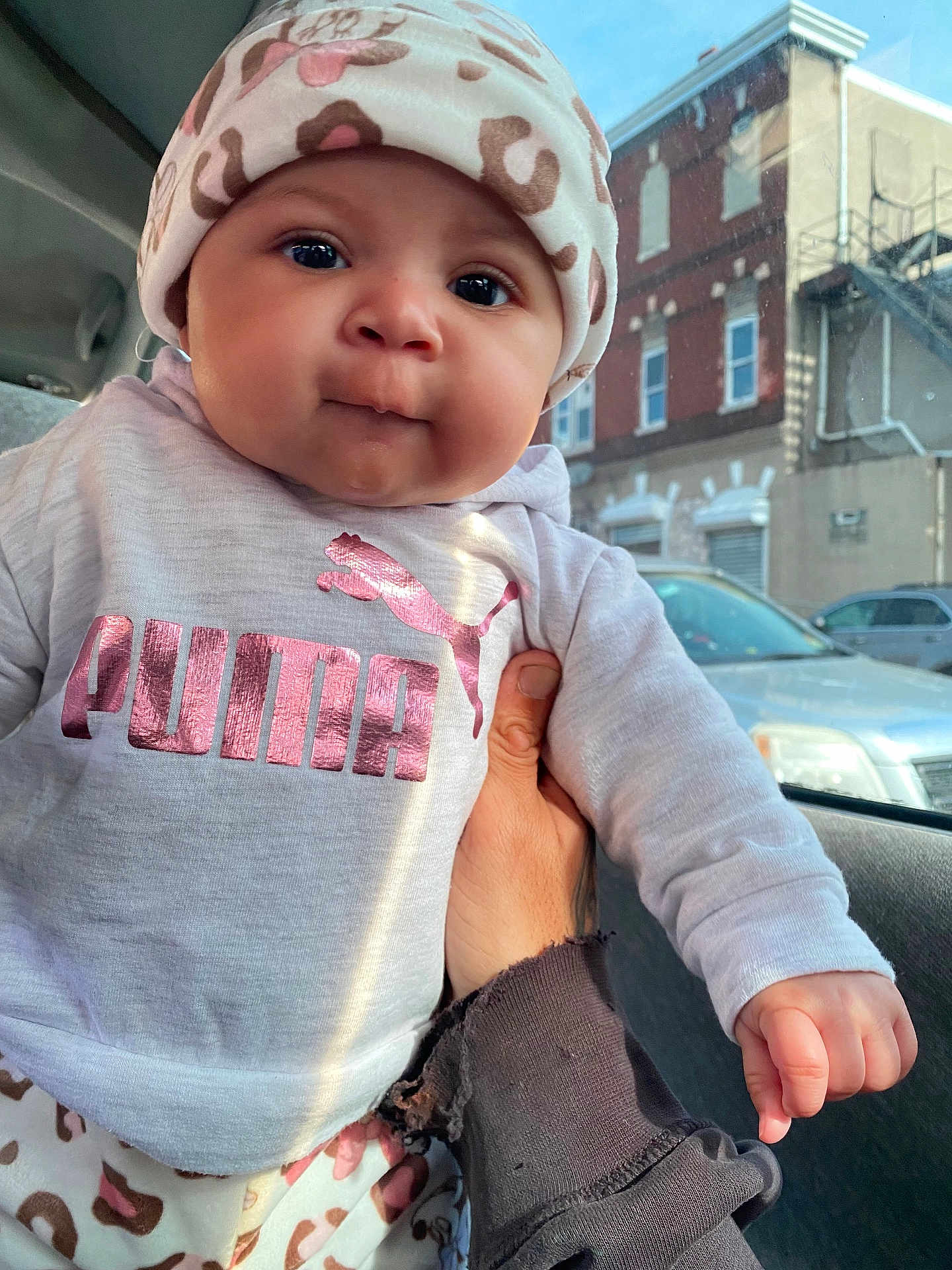 Niyaleii is registered to the contest to win money with this photo: baby, child, infant, hat, clothing, puma, leopard_print, pink, sweatshirt, hand, car, window, city, buildings, daylight, face, portrait, cute, person, casual