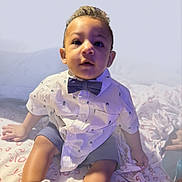 Prince Maki Finney joined the competition — help win amazing prizes! toddler, child, bow_tie, shirt, shorts, sitting, bed, blanket, white_shoes, curly_hair, indoor, portrait, cute, young_child, casual_clothing, person, face, hands, legs, soft_lighting