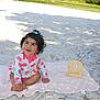 baby, smiling, sitting, blanket, sand, outdoor, watermelon_pattern, curly_hair, child, cute, happy, nature, greenery, park, sunlight, wooden_sign, nine_months, footwear_free, playful, summer