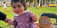 Sophia is registered to the contest to win money with this photo: baby, child, outdoor, grass, swing, playground, cake, birthday, purple_dress, white_bow, smiling, happy, person, sock, table, chair, celebration, toy, fence, daylight