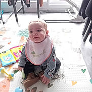 Nolan a rejoint le concours — aidez-le/la à gagner de superbes lots ! baby, child, sitting, bib, toy, play_mat, indoors, clothing, floor, window, furniture, boot, person, cute, colorful, penguin, happy, young_child, soft_toy, home