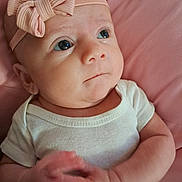 Paisley is registered to the contest to win money with this photo: baby, infant, headband, bow, pink, white_onesie, hands, clasped_hands, face, eyes, expression, closeup, portrait, cute, child, newborn, skin, soft_texture, indoor, blanket