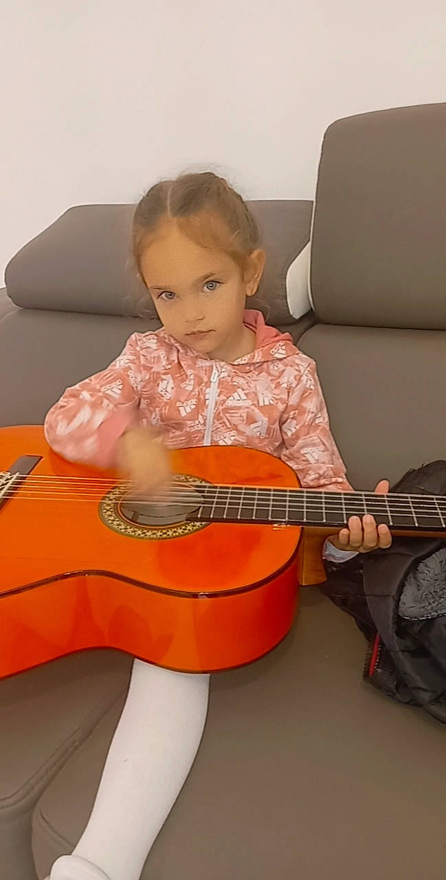 Eleonore a rejoint le concours — aidez-le/la à gagner de superbes lots ! baby_toddler_clothing, comfort, couch, dress, flooring, folk_instrument, guitar, guitar_accessory, hair, lap, music, musical_instrument, musician, orange, person, plucked_string_instruments, string_instrument, string_instrument_accessory, thigh, toddler
