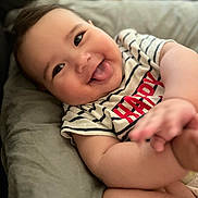 Kayline participe au concours pour gagner de l'argent avec cette photo : arm, baby, casual_clothing, child, chubby_cheeks, closeup, cute, face, happy, indoors, infant, lying_down, playful, portrait, red_text, skin, smiling, soft_surface, striped_shirt, tongue_out