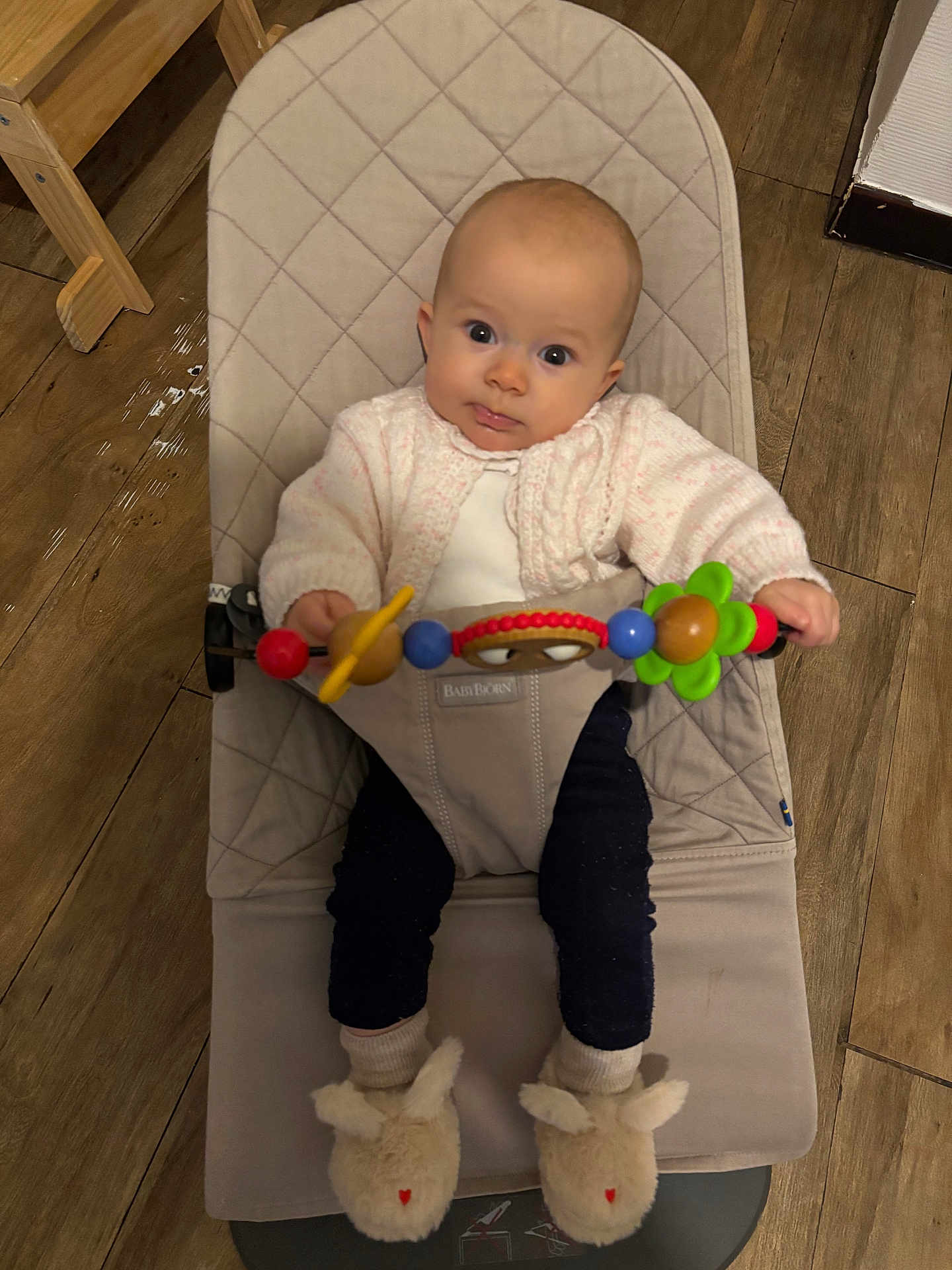 Castille a rejoint le concours — aidez-le/la à gagner de superbes lots ! baby, infant, child, bouncer, toy, colorful_toy, pink_cardigan, bunny_slippers, footwear, wooden_floor, furniture, indoors, seated, cute, curious, wide_eyes, plush, cozy, home, person