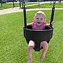 baby, child, swing, playground, green_turf, basketball_hoop, sunlight, happy, smiling, toddler_swing, red_dress, outdoor, park, baby_clothing, person, barefoot, summer, fun, play, joy