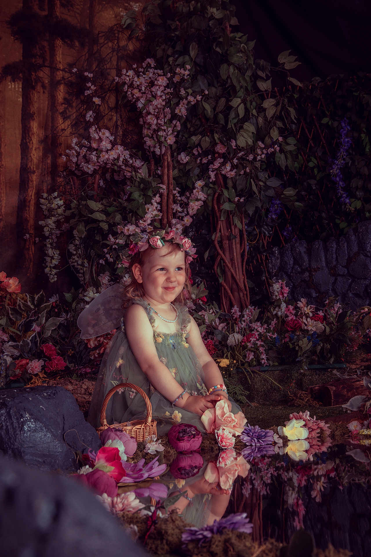 Erica is registered to the contest to win money with this photo: child, girl, fairy, flower_crown, wings, dress, smile, pond, reflection, flowers, greenery, nature, garden, sitting, portrait, bracelets, basket, magical, fantasy, cute