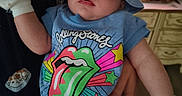 Skyla is registered to the contest to win money with this photo: apparel, baby, blue_hat, child, closeup, colorful_clothing, curious_expression, cute, hand, headwear, holding, indoor, infant, mittens, onesie, person, portrait, rolling_stones, soft_lighting, wide_eyes