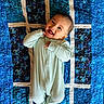 baby, infant, smiling, onesie, quilt, blue, pattern, happy, lying_down, child, cute, portrait, fabric, textile, home, cozy, small_person, cheerful, toddler, background