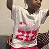 Marsai is registered to the contest to win money with this photo: beads, blurry, braided_hair, candid, casual, child, cute, family, girl, indoor, patterned_clothing, person, pink_skirt, portrait, raising_hands, snapshot, sofa, text_overlay, wall, white_shirt