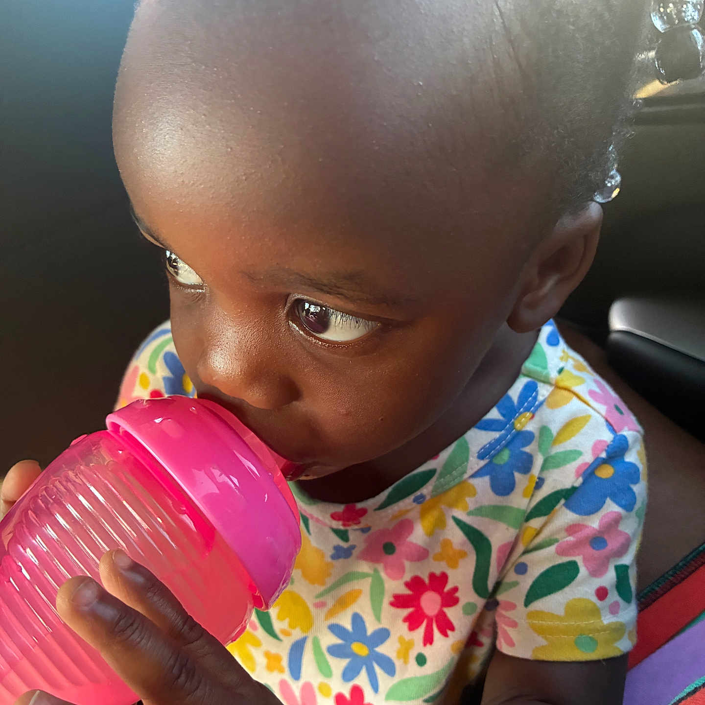 Marsai is registered to the contest to win money with this photo: toddler, child, sippy_cup, drinking, colorful_clothing, floral_pattern, cute, indoors, portrait, baby, hand, face, skin, hair, curious, bright, natural_light, closeup, young, casual