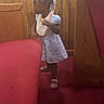 Marsai joined the competition — help win amazing prizes! child, toddler, girl, standing, beaded_hair, bib, dress, shoes, red_cushion, bench, wood_paneling, carpet, indoor, furniture, room, motion_blur, side_view, young_child, casual_clothing, candid